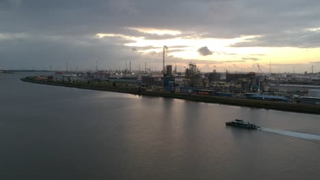 Edificios-Industriales-Del-Puerto-De-Amberes-Mientras-Un-Pequeño-Barco-Navega,-Vista-Aérea