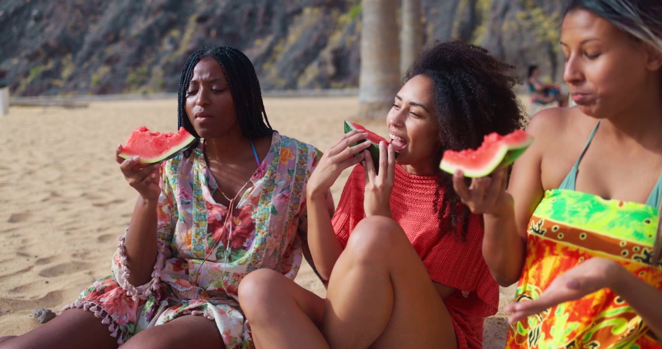 Mujeres diversas felices comiendo sandía en una playa soleada