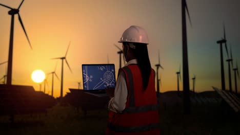 back view of asian female engineer in a helmet looking at the wind turbine blueprint on the laptop while standing in front of wind turbines rotating at sunset