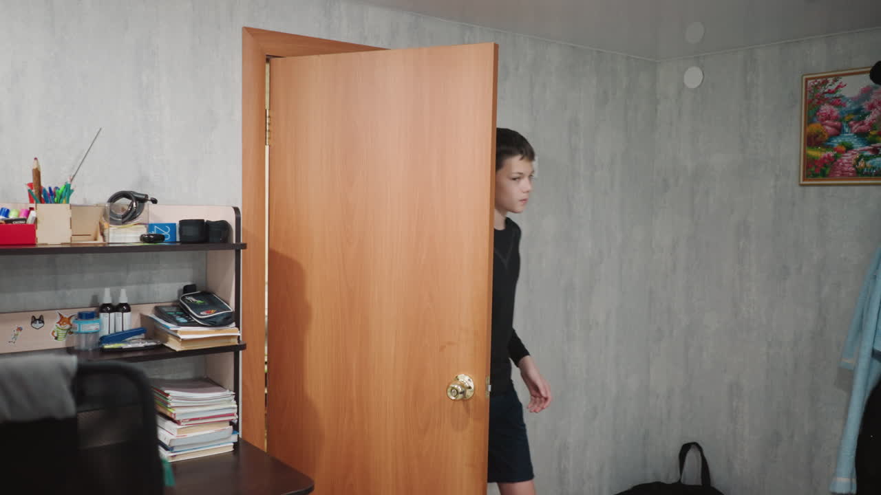 Young white grandson opens wooden door into study, curious gaze, cluttered shelf and desk with books, casual shirt and shorts, soft morning light, candid family moment of exploration and playful mood