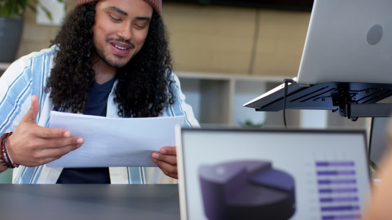 Homem asiático segurando um relatório de gráfico de barras impresso, explicando dados para colega digitando um gráfico de pizza no laptop