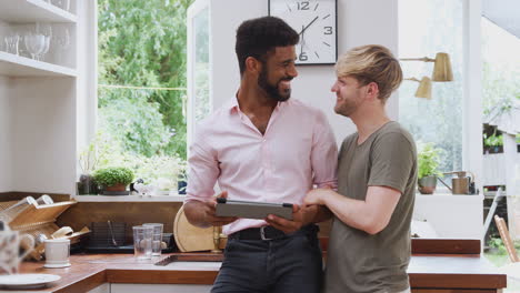 male gay couple using digital tablet at home in kitchen together