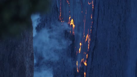 pequeñas fuentes de lava en el borde del lago de lava en la erupción de kilauea de 2022 con vapor y ramas de árboles en primer plano