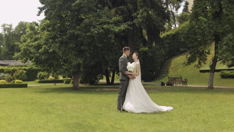 Newlyweds,-caucasian-groom-with-bride-walking,-embracing,-hugs-in-park,-wedding-couple