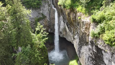 Waterfall-cascading-down-rocky-cliffs-surrounded-by-lush-forest-in-Glarus-Süd,-Switzerland