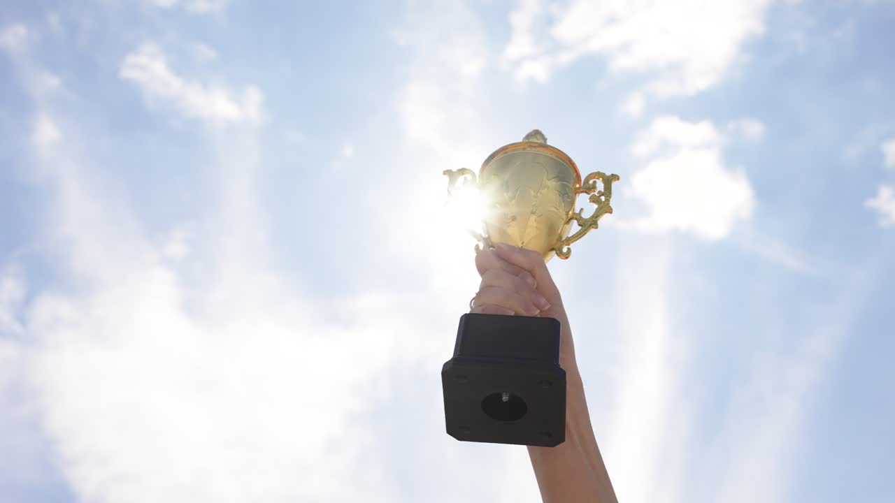 Raised hand holding trophy against sky in outdoor setting. Concept of achievement, success, victory, motivation, and recognition. Symbol of excellence and winning spirit