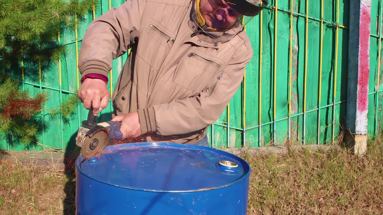 un hombre está cortando un barril de metal azul con una molienda angular.