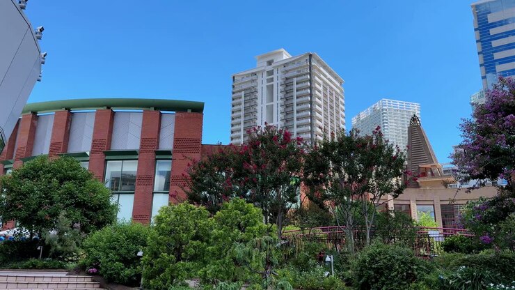 Paesaggio urbano moderno con vegetazione lussureggiante e grattacieli sotto un cielo azzurro brillante
