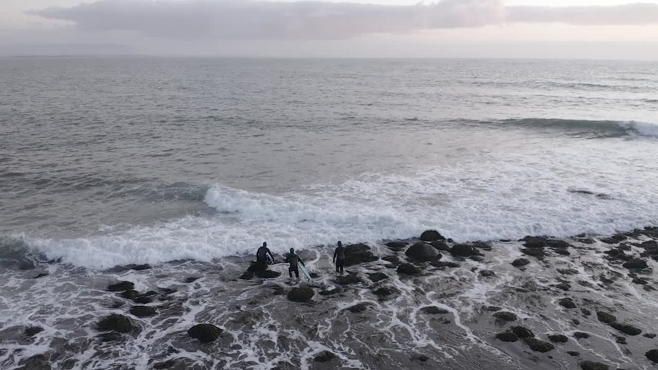 아이슬란드의 차가운 물에서 바위가 많은 쇼어브레이크를 통과하려는 서퍼들, 공중