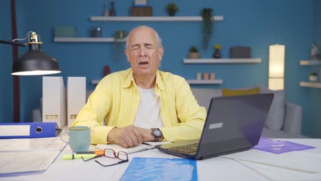 home office worker old man yawns and relaxes at the camera.