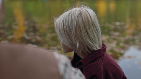 young blonde boy drinking from a mug outdoors near a lake