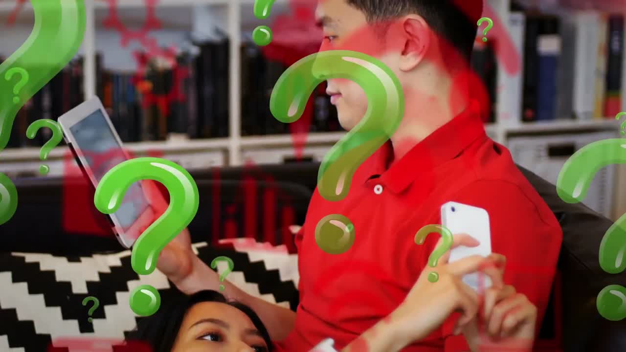 вопросительный знак и цифровые значки, плавающие против азиатской пары, использующей электронные устройства дома