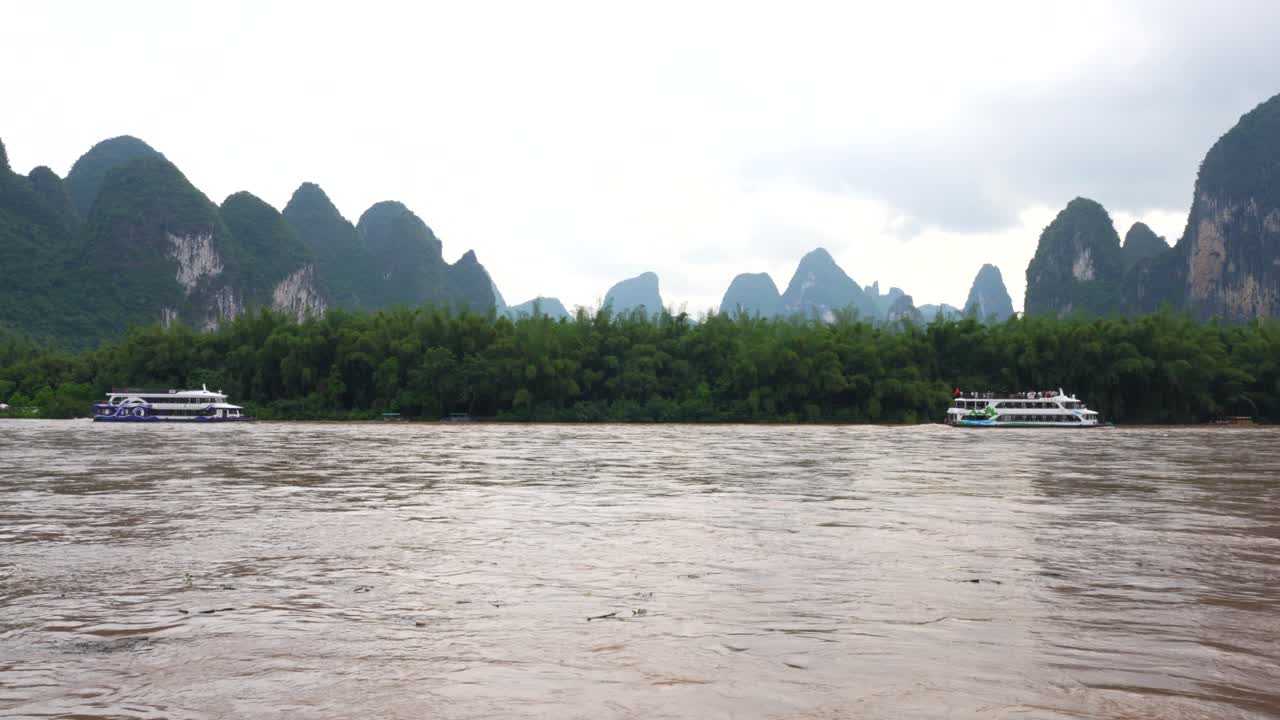 cruceros en el río li con aguas marrones, rodeado de montañas cársticas