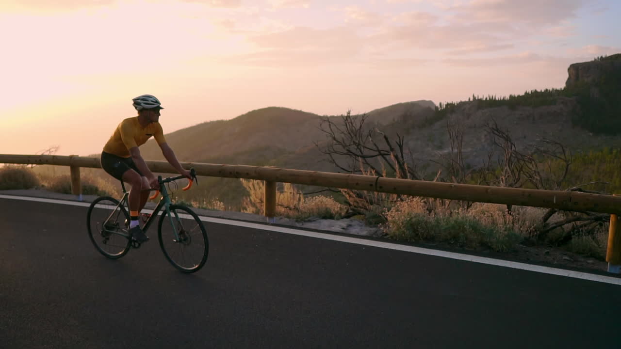 The athlete on a bike rides a mountain serpentine in slow motion, relishing the island's view, epitomizing a dedication to a healthy lifestyle at sunset