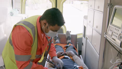 male paramedic with face mask using stethoscope on an american patient in the ambulance