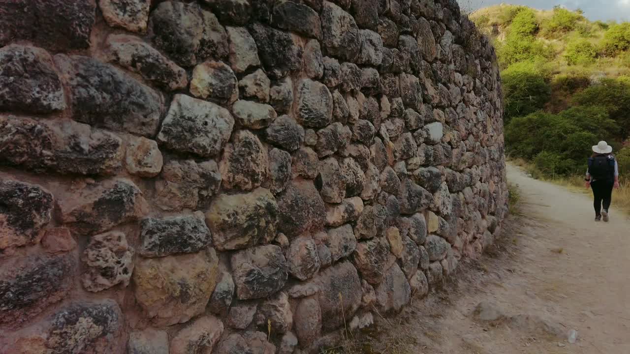 Young woman walks on trail alongside K'allachaka ruins outside the city of Cusco. Old inca trail surrounded by andean vegetation