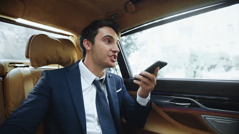 hombre de negocios exitoso grabando un mensaje de voz en un teléfono inteligente en un coche moderno.