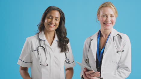 retrato de una doctora y una enfermera con una bata blanca de pie frente al fondo azul del estudio