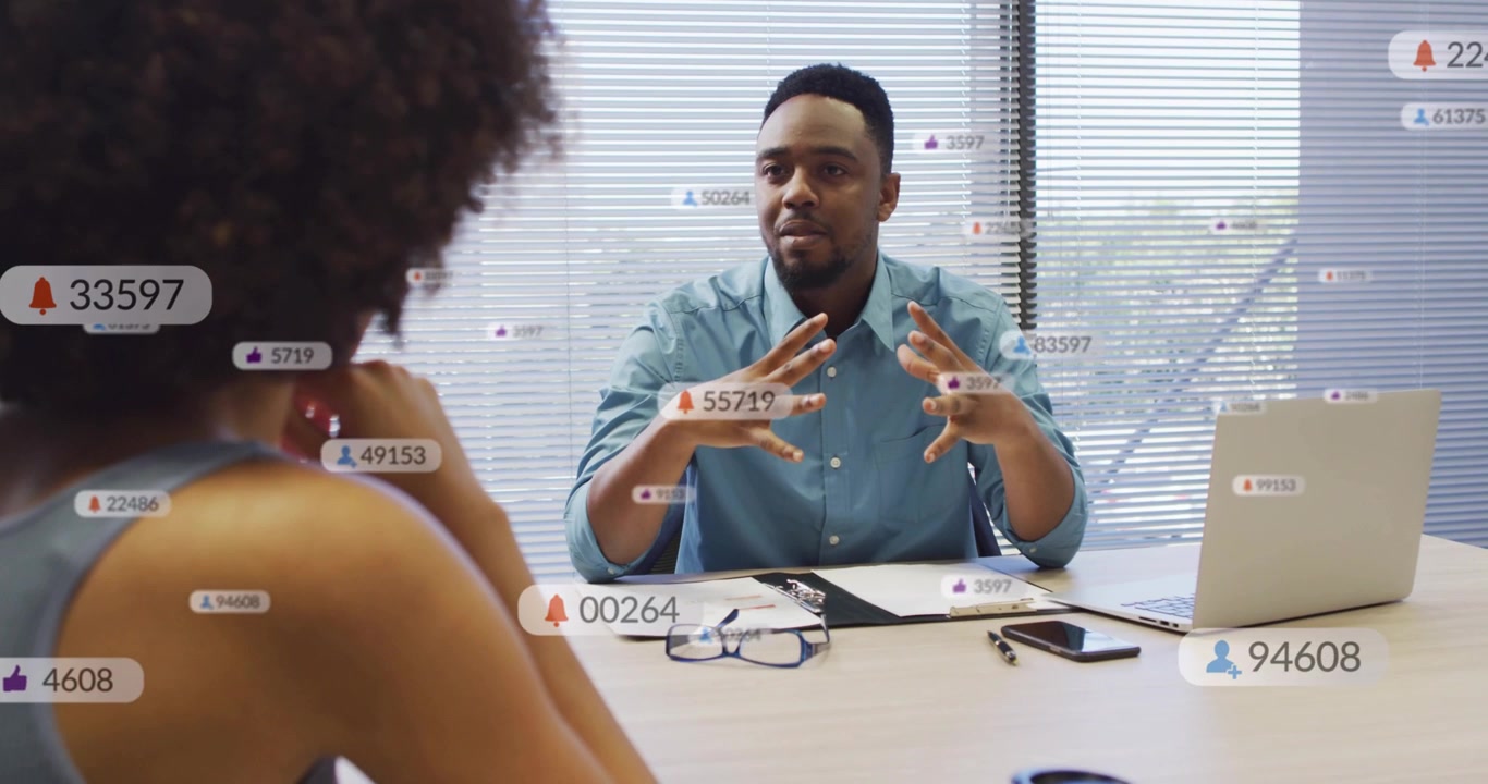 Man speaking and gesturing at table, causing badges rising over laptop, showing analytics