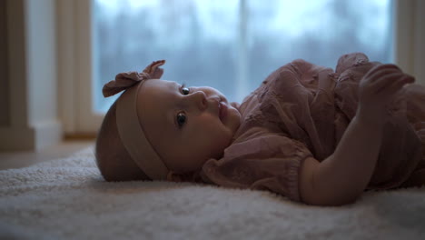 Close-ground-side-view-of-adorable-baby-lying-on-carpet-on-floor