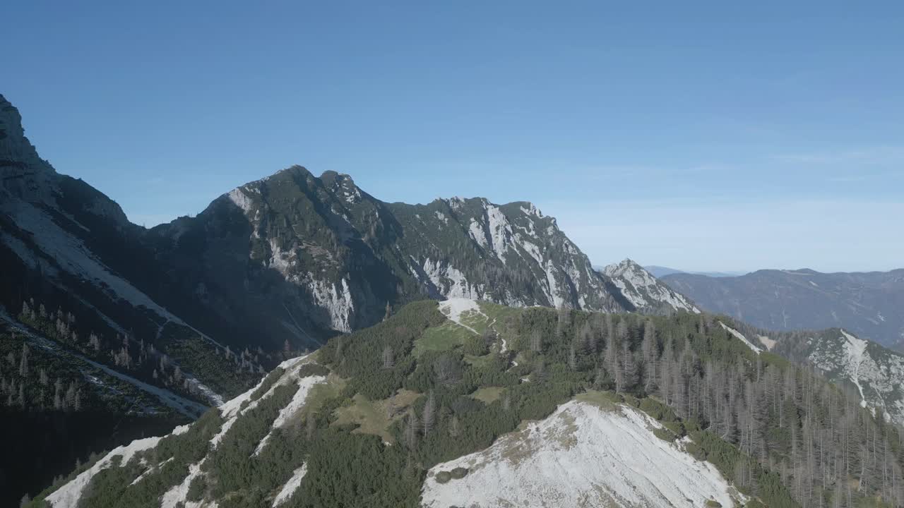 Drone view of Mangart Mountains, Slovenia: jagged peaks, rugged cliffs, lush green valleys, winding alpine roads, dramatic landscape, clear skies, Julian Alps, untouched natural beauty
