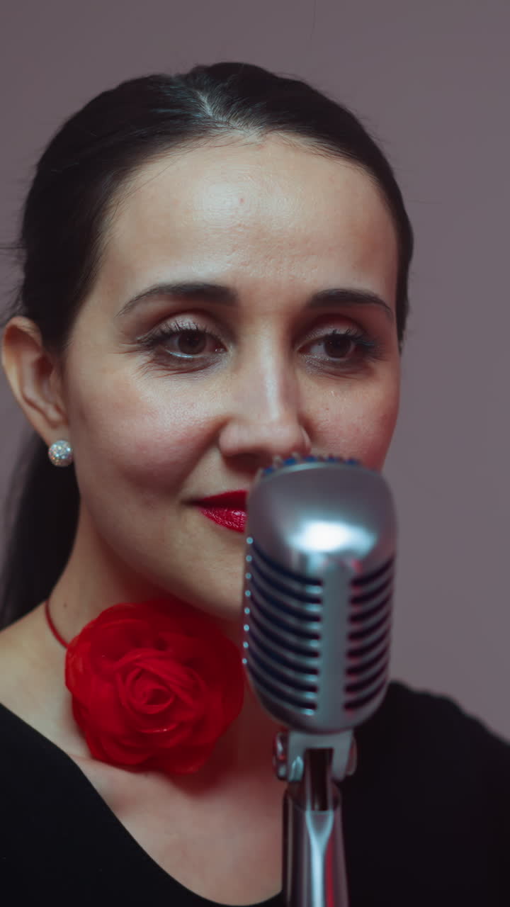 una cantante concentrada se para con confianza frente a un micrófono vintage con las manos en la cintura. su expresión decidida y su elegante traje negro