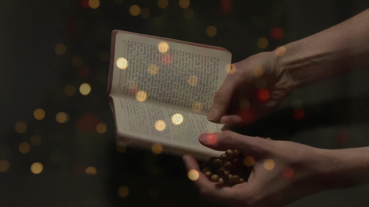 Animazione di sfere di luce su mani che tengono Bibbia e rosario su sfondo nero