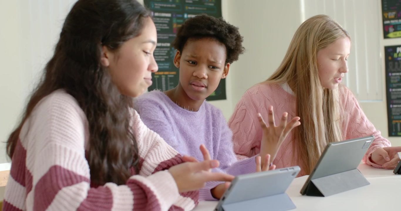 Diverse teen females helping after center student vocalizing confusion, tapping tablets at school