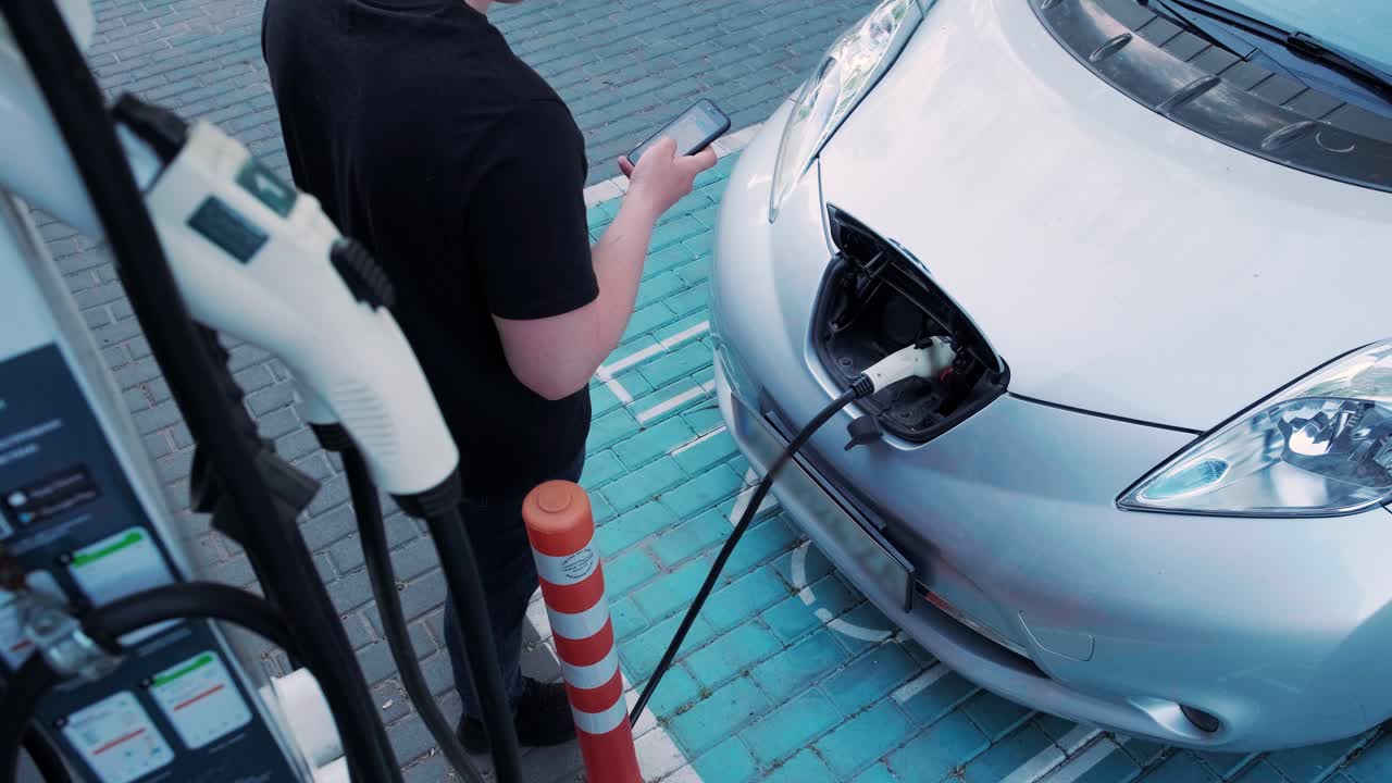 전기 자동차의 연료 충전 과정: 전기 에코 자동차가 충전하는 치 아래의. 전기 자동차 충전 치는 자동으로 열립니다. 남성 손이 발기 된 자동차를 입합니다.