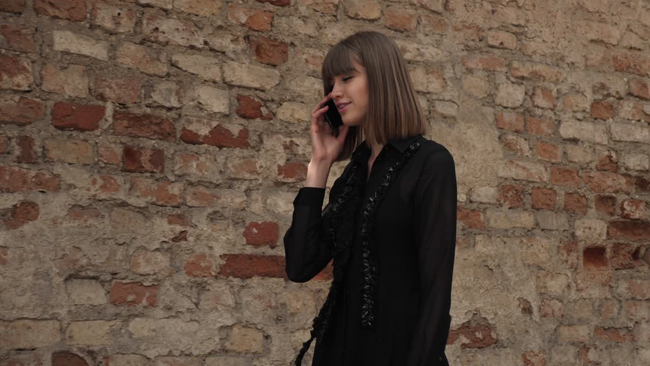Young woman walking in old town street while talking on phone, expressing joy