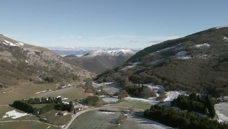 Drone view over Valsorda, Gualdo Tadino, on a sunny winter day. Snow-dusted peaks rise above a vibrant landscape, blending crisp white and rich earthy tones under a clear blue sky