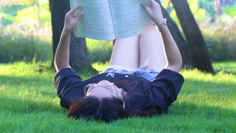 real shot girl is lying and reading her favorite book on a green meadow park covered with yellow flowers in a nice sunny summer, spring day