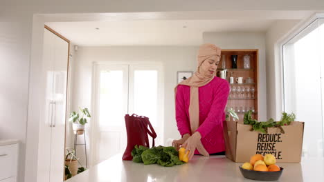 biracial woman in hijab with grocery shopping in kitchen at home with copy space, slow motion