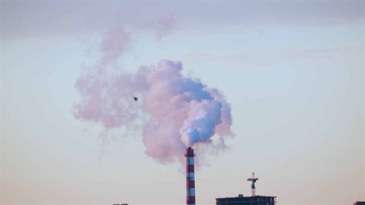 Ciminiera industriale che rilascia fumo denso nel cielo sopra un cantiere edile cittadino.