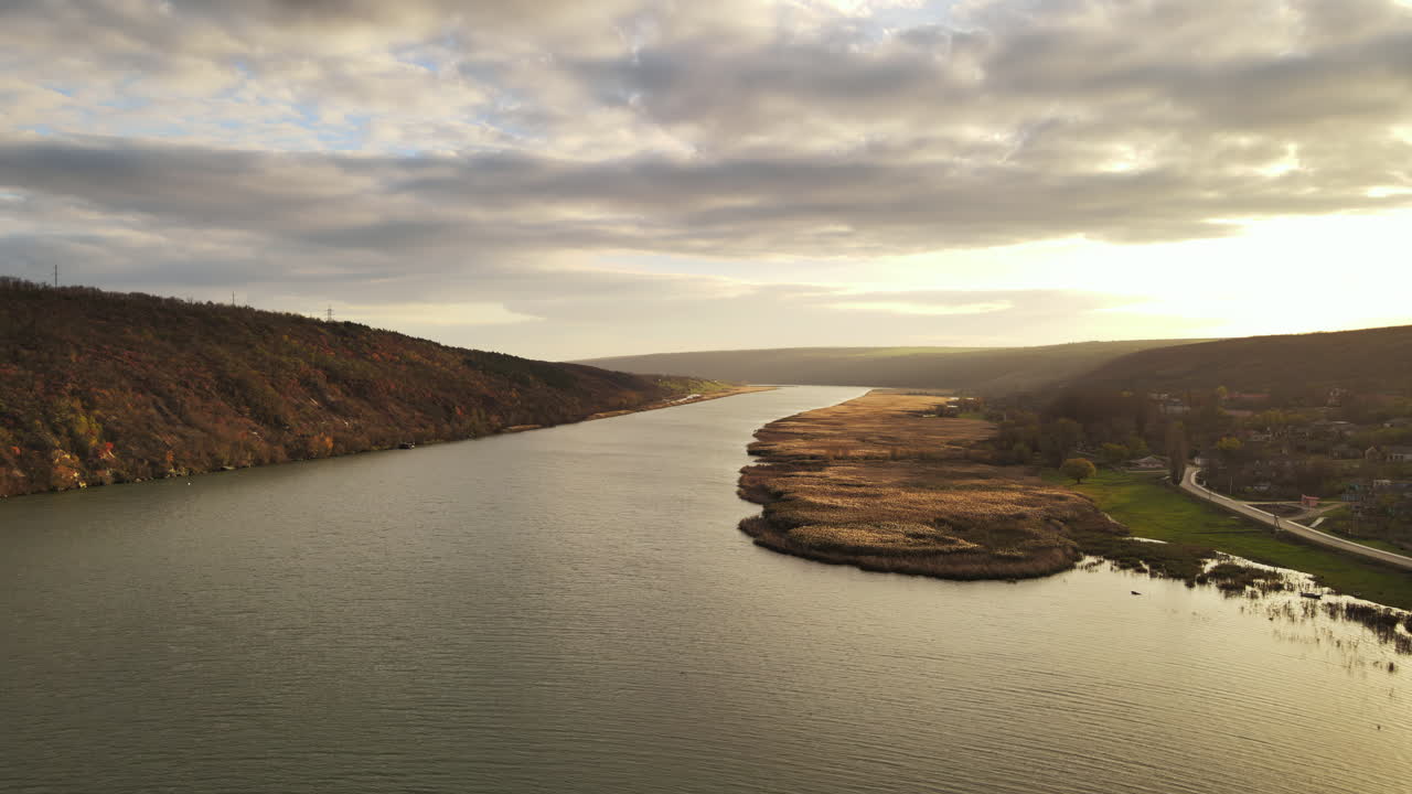 Majestic river flows gently through a stunning autumn scene. Beautiful colors warm the landscape as the sun rises, illuminating the tranquil countryside atmosphere