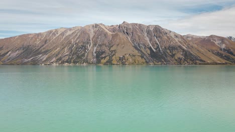 Rocky-face-of-mountain-behind-turquoise-glacial-lake-in-sunshine