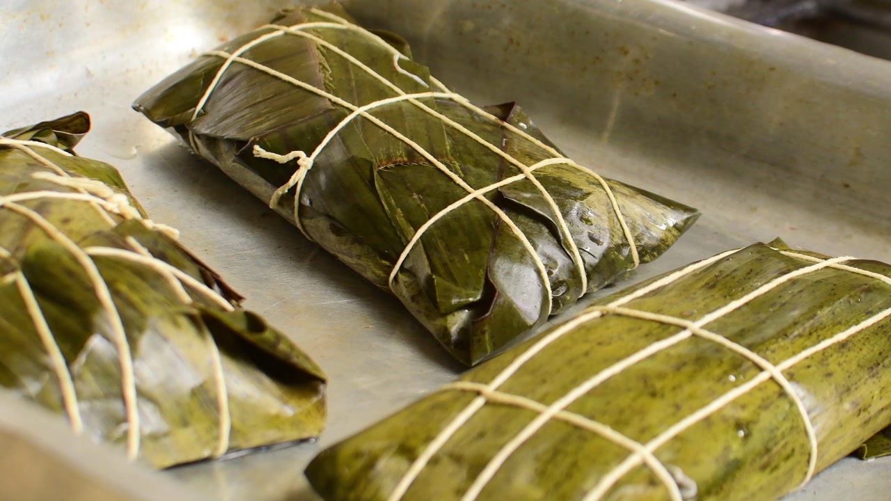 Three Venezuelan Hallacas wrapped in banana leaves on a metal tray