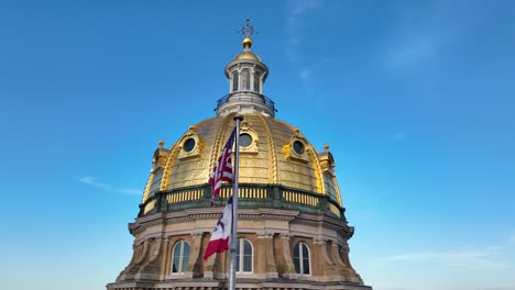 bandeiras da américa e de iowa a acenar em frente à cúpula do capitólio em des moines, ia.