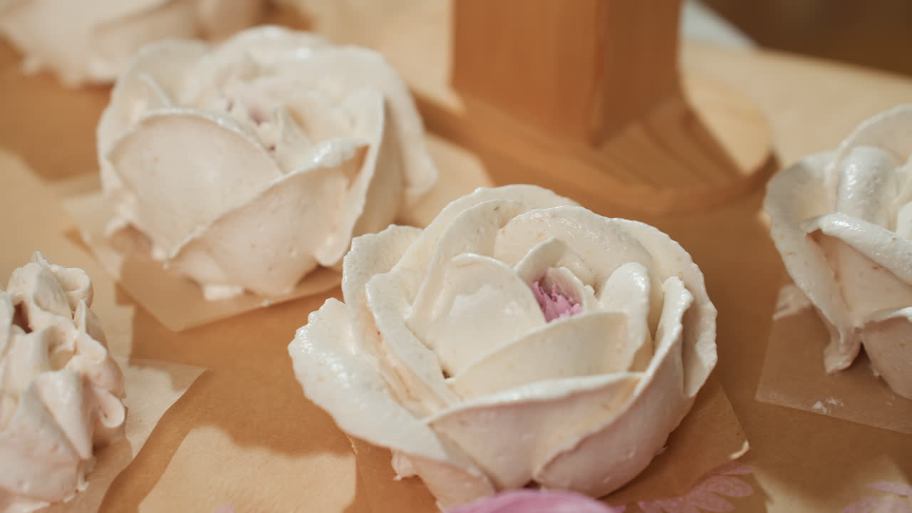 Close up of beautifully arranged flower-shaped white frosting cakes with hints of pink centers resting on parchment paper, showcasing intricate piped design and dessert decoration ready for baking