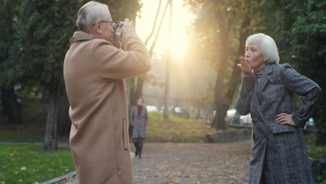 elderly man taking a photo with smartphone camera of his lovely grey haired wife in the park in autumn