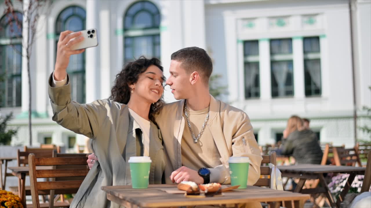 Una coppia felice all'aperto vicino a un bar. Selfie, baci, caffè sul tavolo, il loro cane nelle vicinanze. Atmosfera autunnale. Rallentatore