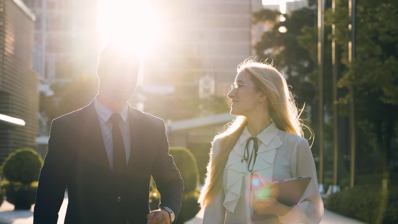 Smiling businessman and business woman talking on the go in setting sun sunlight, slow motion