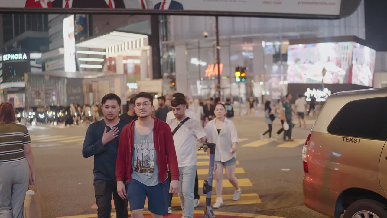 Slow motion shot of locals and visitors crossing road at Kuala Lumpur city in Malaysia. Advertising Billboards.