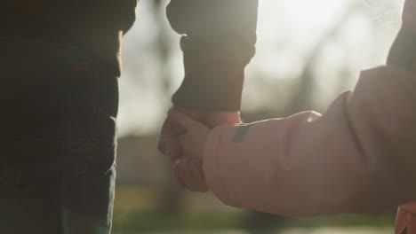 close-up back view of a little girl in a pink jacket holding hands with a man in a brown jacket, both wearing blue jeans, walking together