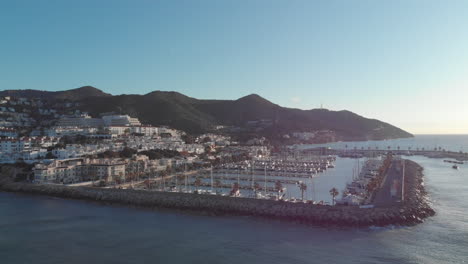 Aerial-drone-ascending-pier-with-port-yachts-,-reveals-blue-horizon-during-sunset