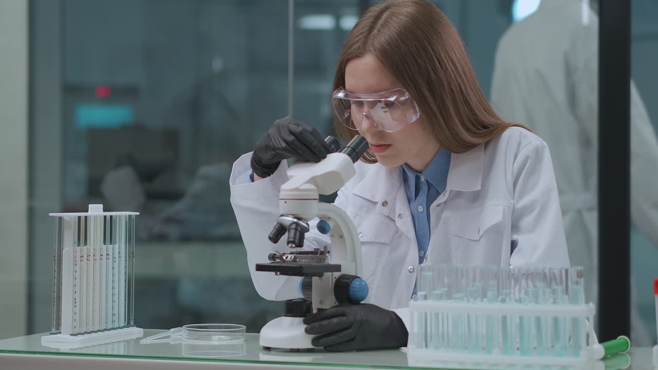 young female health professional is working in laboratory testing new vaccine from covid-19 using modern microscope medical and virology analysis