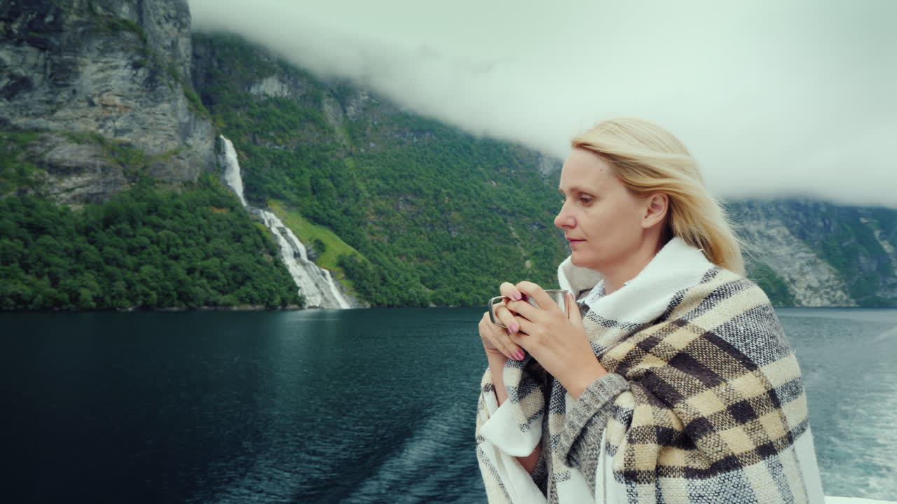 유람선에서 손에 차 한 잔을 들고 있는 한 여성이 아름다운 산을 바라보고 있습니다.