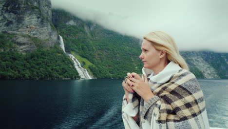 a woman with a cup of tea in her hands aboard a cruise ship looks at the beautiful mountains of the