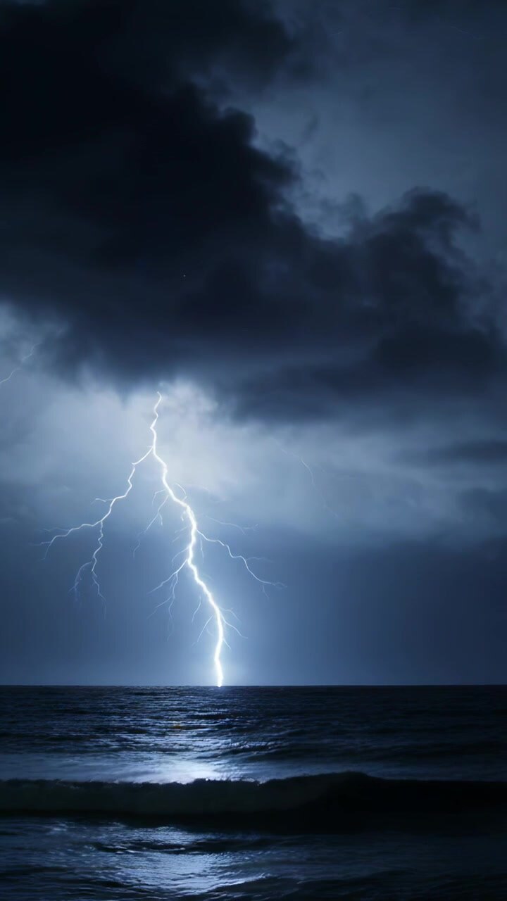 Video verticale: Nuvola che accumula carica, un fulmine a saetta che colpisce il mare aperto di notte, illuminando le onde.