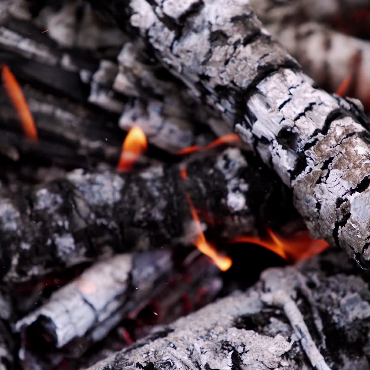 Motion of wooden logs in fire. Wooden stick turning over smoldered logs. Glowing firewood. Close-up.